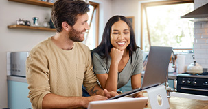 a couple looking at their laptop computer in their kitchen