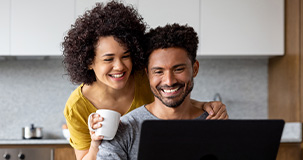 A smiling couple looking at a screen in their kitchen.